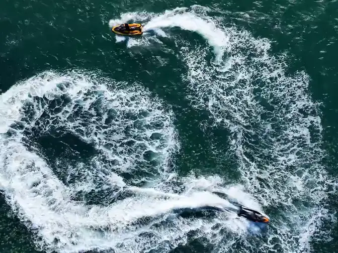 Two jet skis carving spirals and wakes off Terrigal, with The Skillion behind