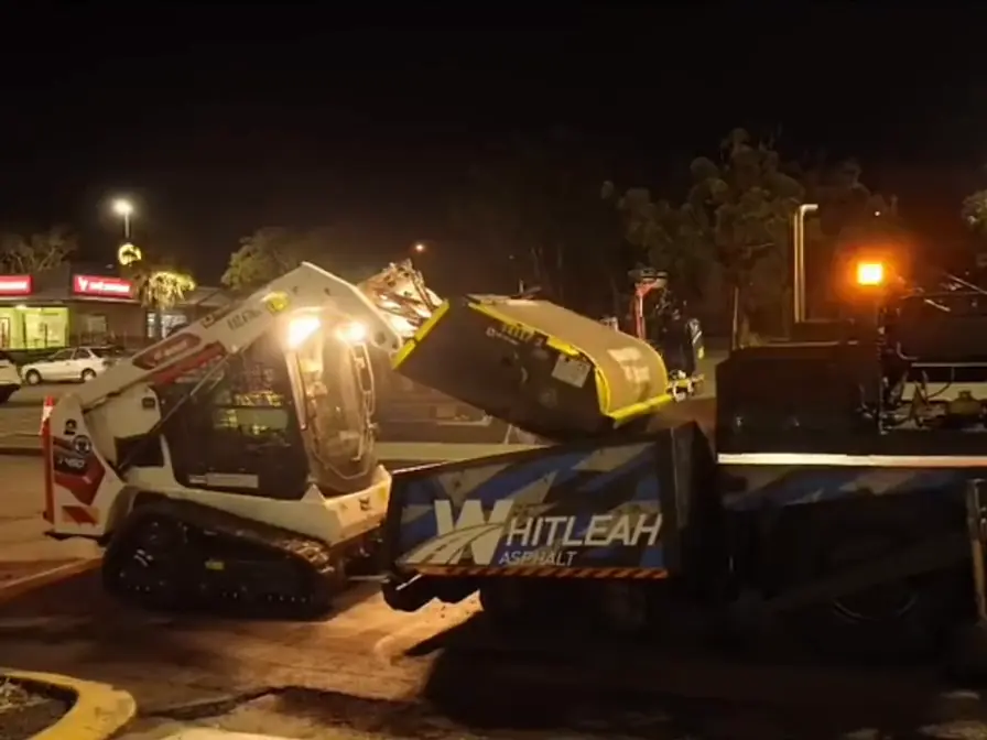 Night road works by Whitleah Asphalt: a profiler loading a truck and a skid steer filling a paver under work lights